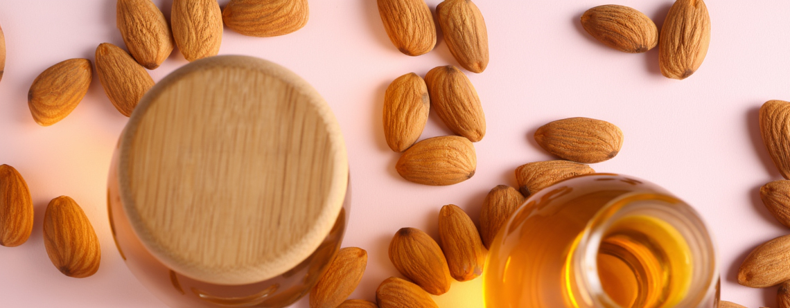 Olio alle mandorle dolci in flacone, circondato da mandorle intere su sfondo naturale